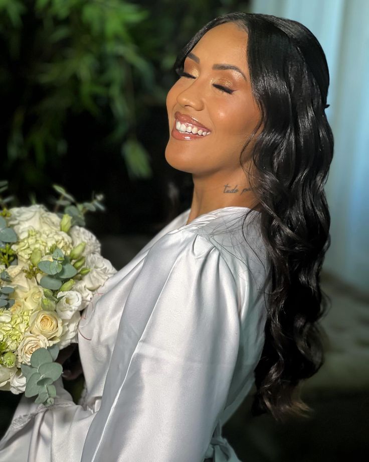 Noiva com maquiagem profissional, cabelos longos, robe acetinado e buquê branco